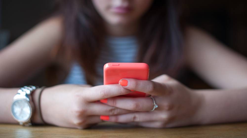 Teenage girl sitting at a table holding an orange smart phone.