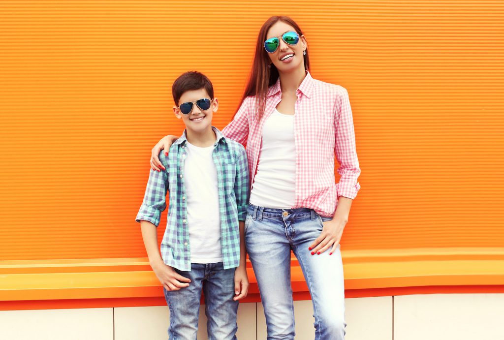 Happy mother and son teenager wearing a checkered shirt and sunglasses in city over orange background