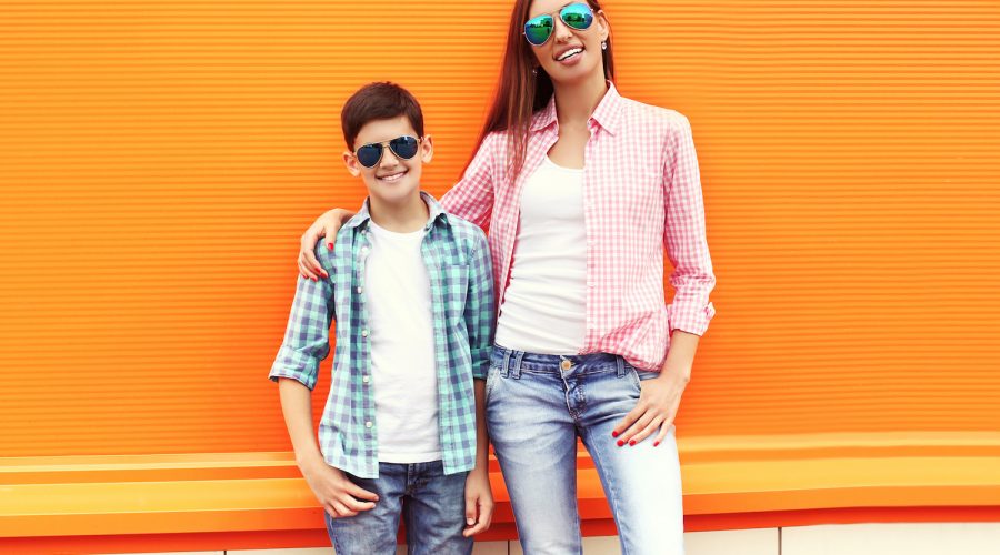 Happy mother and son teenager wearing a checkered shirt and sunglasses in city over orange background
