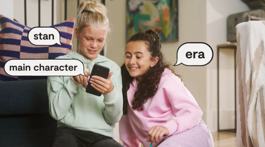 two teen girls looking at a smartphone, speech bubbles with popular slang words