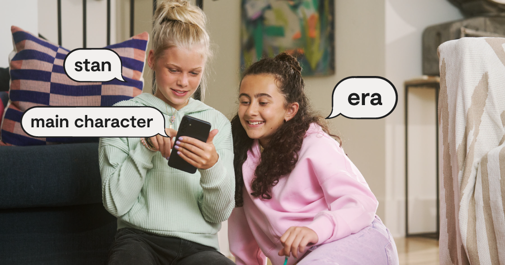 two teen girls looking at a smartphone, speech bubbles with popular slang words