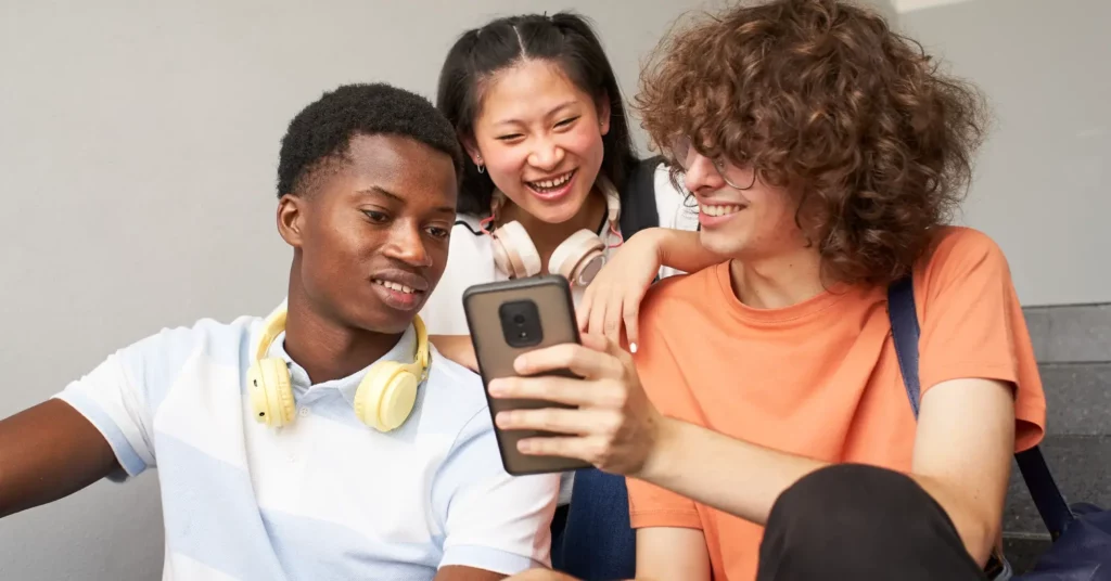 three teens looking a smartphone together