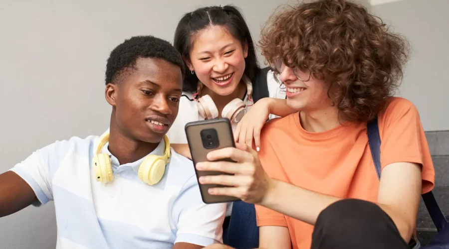 three teens looking a smartphone together