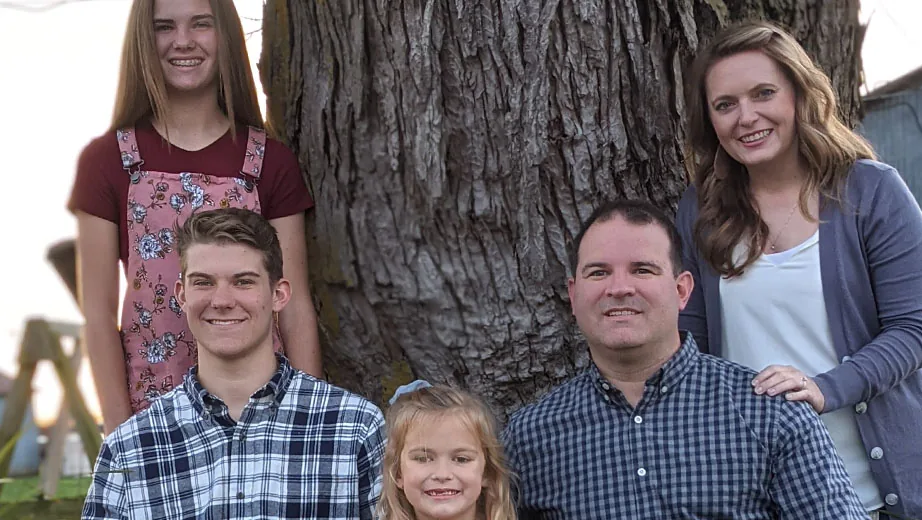 Family of five posing outdoors by a tree