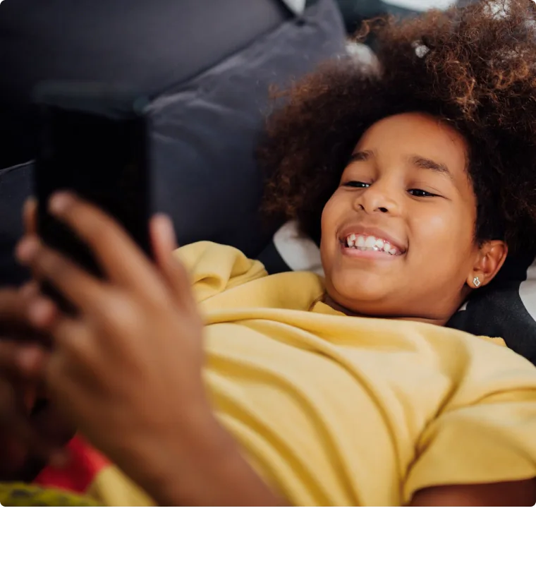 Child lying on a couch looking at a phone