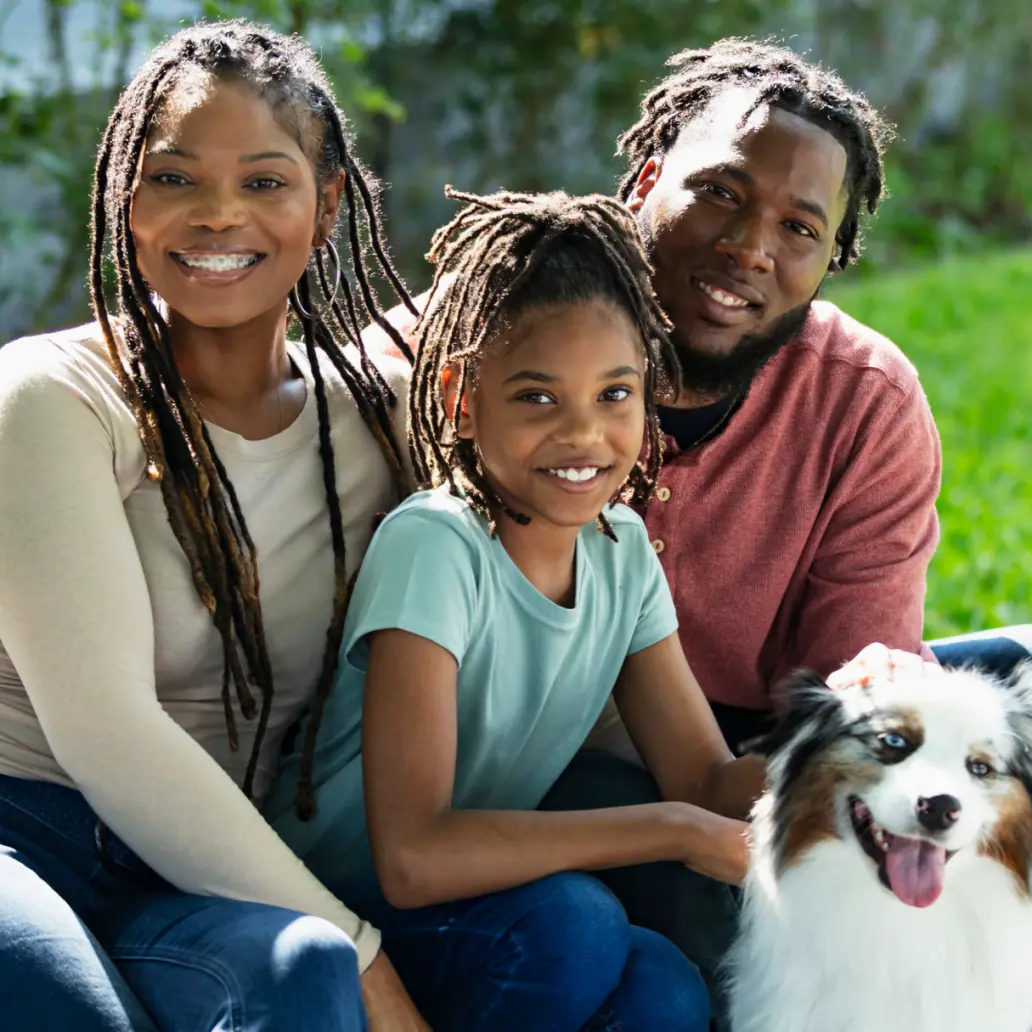 Smiling family of three sitting outside with their dog