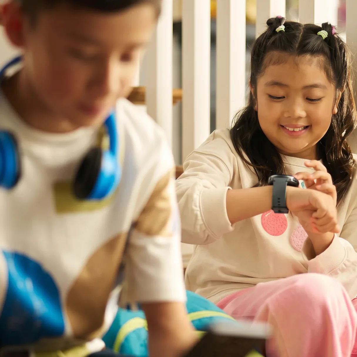 Young girl checking her Bark Watch while her older brother sits beside her with headphones